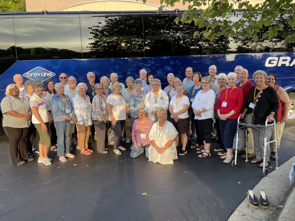 A large group of senior adults posing together in front of a bus on a quarterly trip